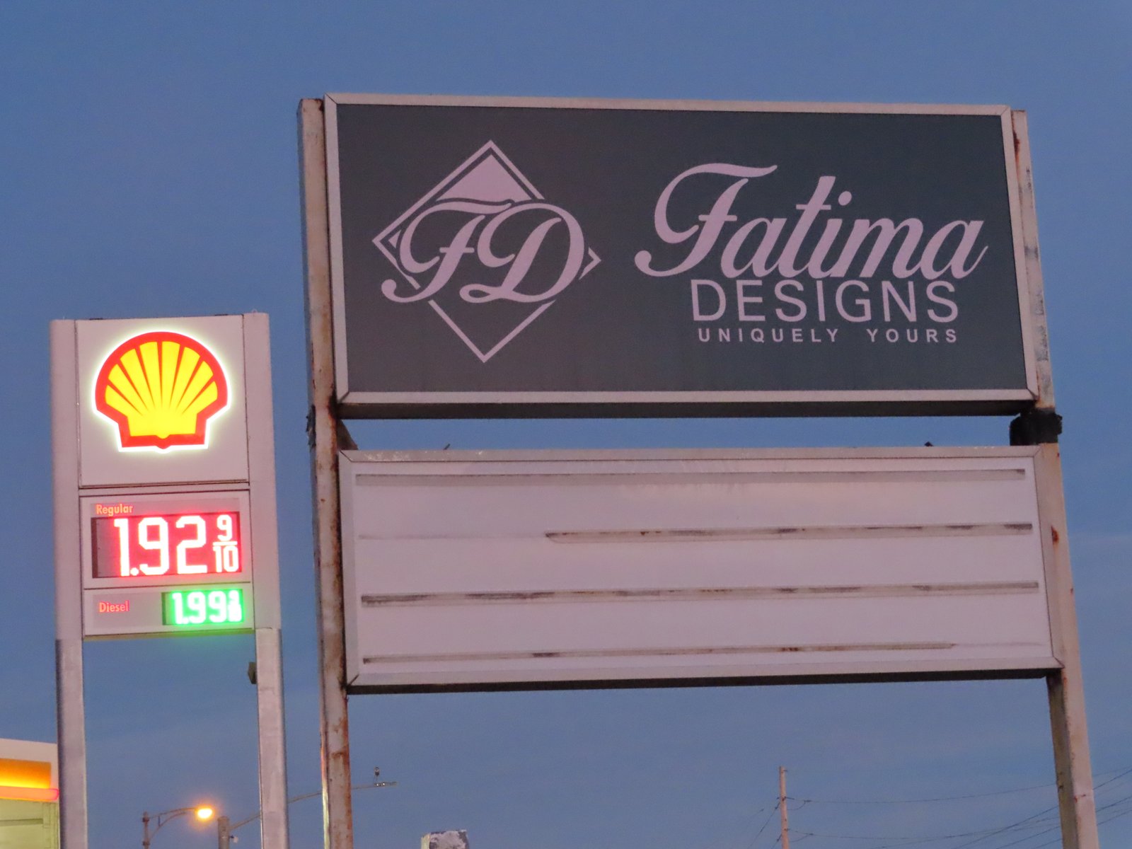 Fatima Designs sign with gas station sign in the background showing $1.92 for a gallon of gas.